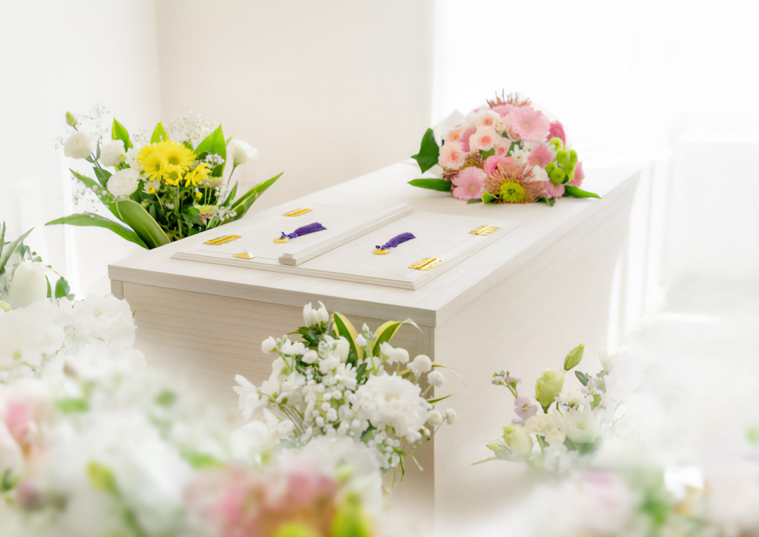 棺が置かれており、周りには白やピンクなどの花で作られた花束が置かれています