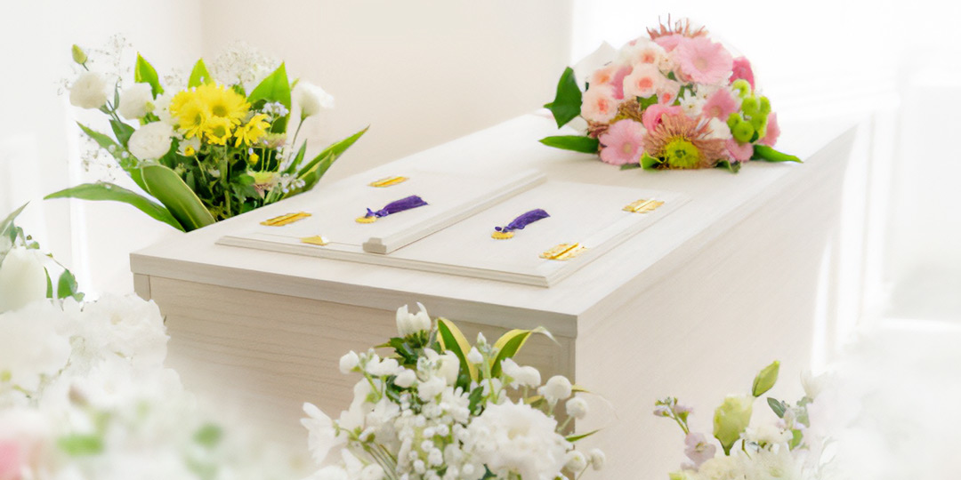 棺が置かれており、周りには白やピンクなどの花で作られた花束が置かれています