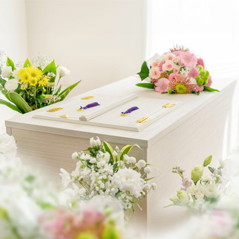 棺が置かれており、周りには白やピンクなどの花で作られた花束が置かれています