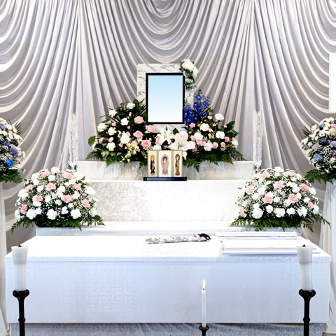 白やピンク、紫などの花で作られた祭壇と、その横にはスタンドの花が置かれ、手前には棺が置かれています